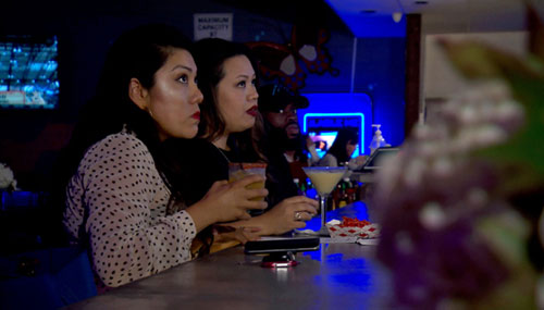 Dos mujeres latinas sentadas en un bar y bebiendo cócteles en Novocane Bar and Grill
